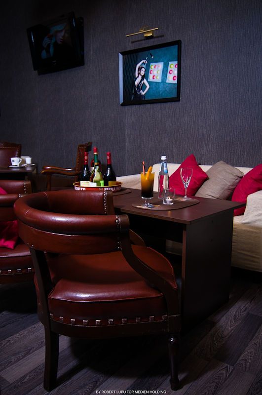 Cozy lounge seating area with leather chairs, cocktails, and poker artwork on dark textured walls.