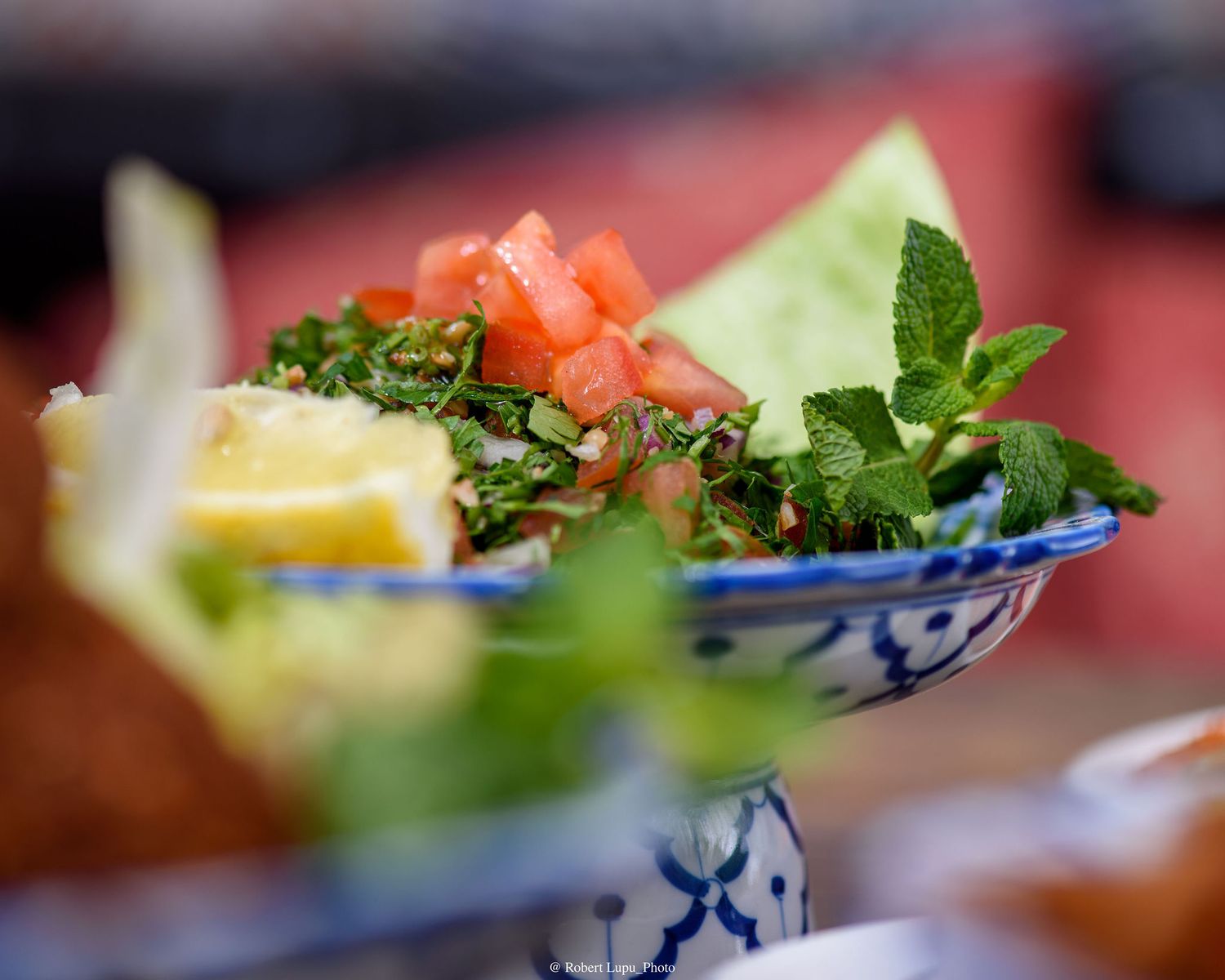 Fresh tabbouleh salad with diced tomatoes, parsley, and mint leaves served in a decorative blue and white bowl.