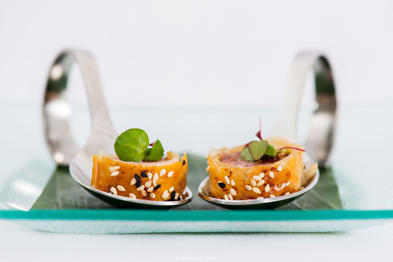 Two elegant appetizer spoons with salmon tartare, sesame seeds, and microgreens served on a glass tray.