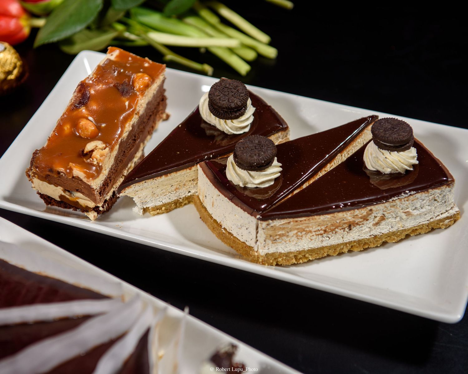 Elegant dessert plate with chocolate-glazed cheesecake slices topped with Oreo cookies and cream rosettes on white platter.