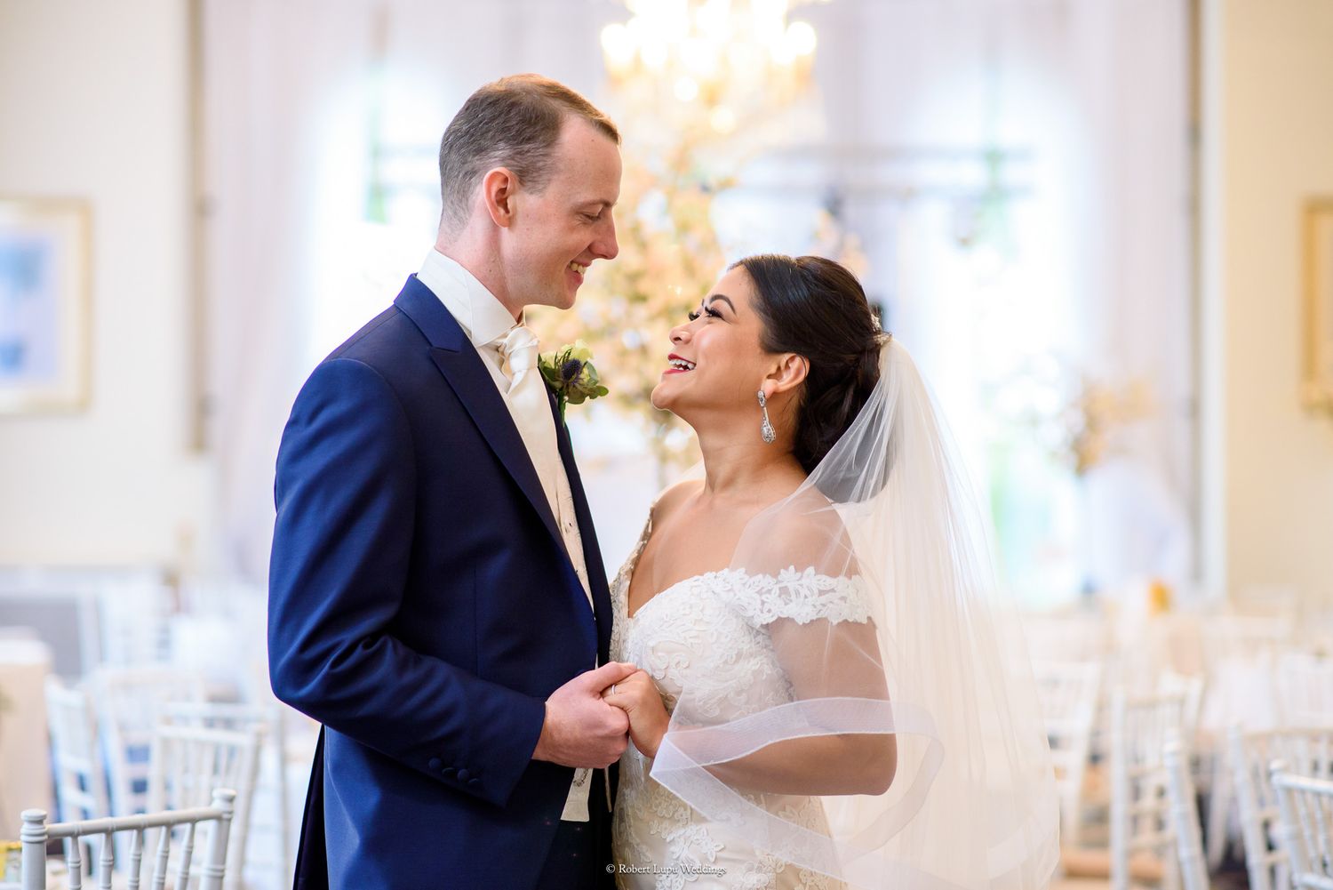 Bride and groom share a romantic moment in an elegant wedding venue, with the bride in a lace gown and veil.