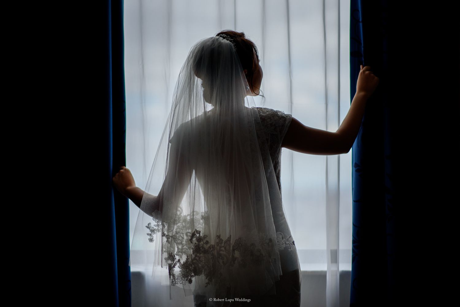 Silhouette of a bride in a veil standing at a window, gazing outside on her wedding day.