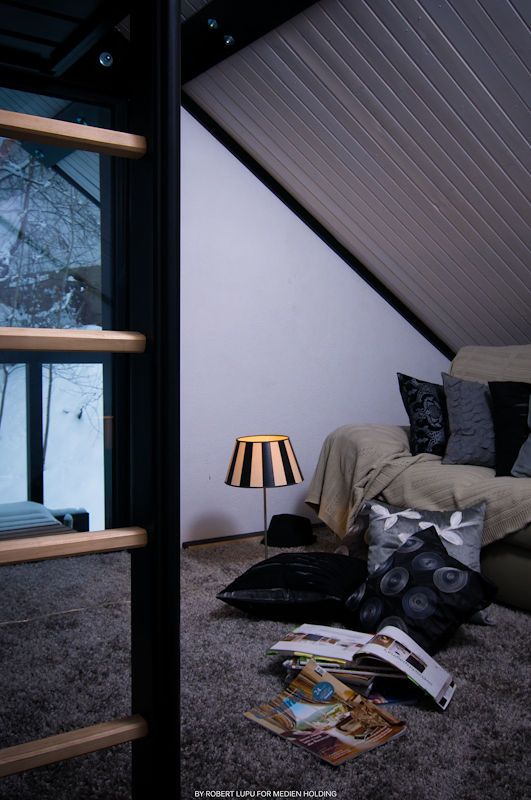 Cozy attic bedroom with slanted ceiling, striped lamp, scattered magazines, and decorative pillows in moody evening lighting.