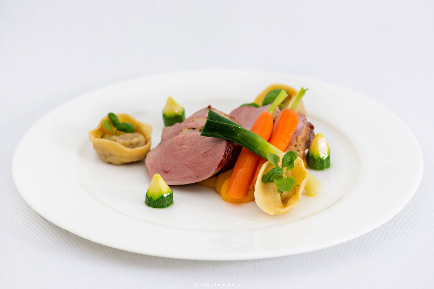 Elegant plated dish with sliced duck breast, glazed carrots, zucchini, and garnished pastry on a white plate.