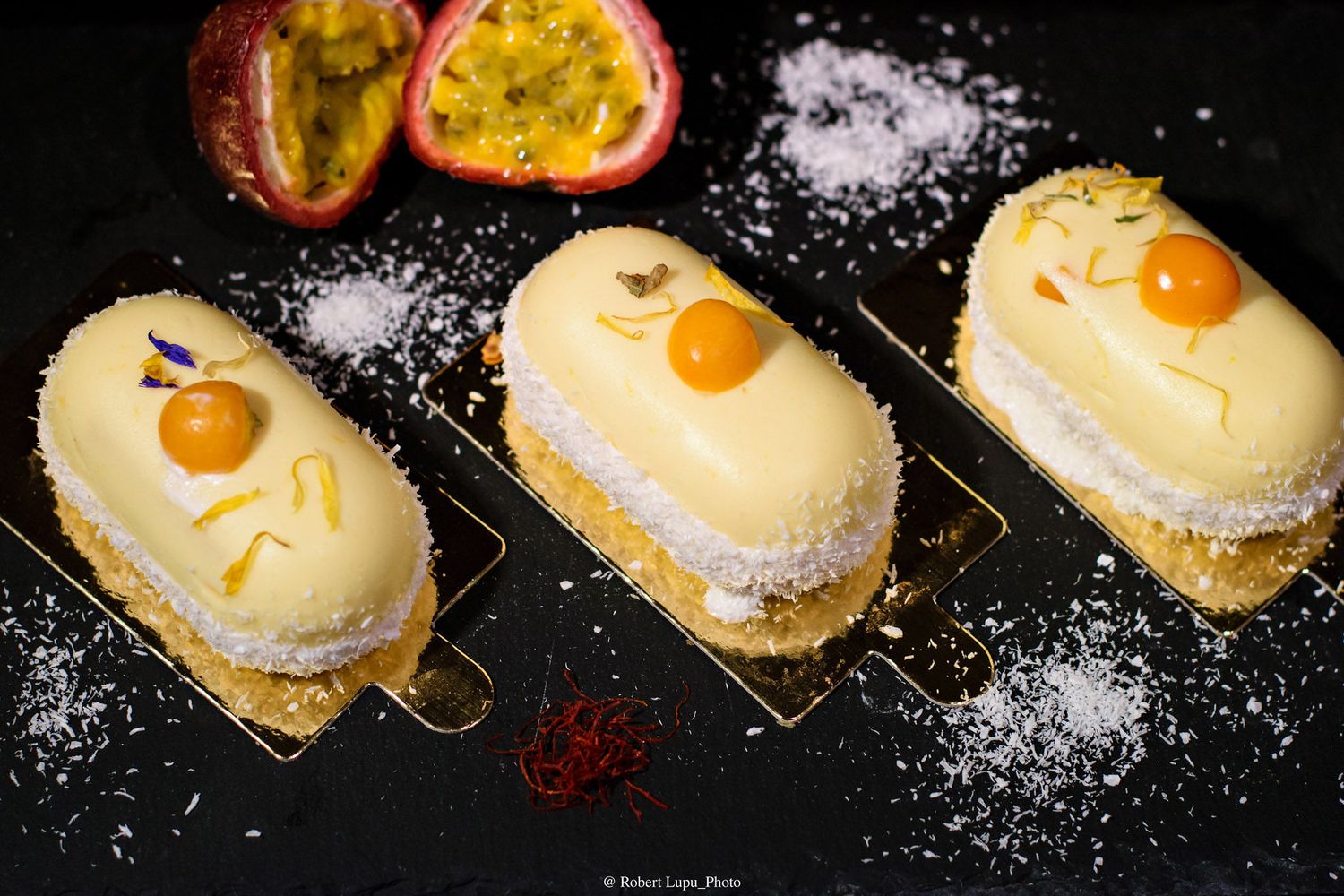 Three elegant passion fruit eclairs topped with white chocolate glaze, coconut flakes, and fresh passion fruit on a dark surface.