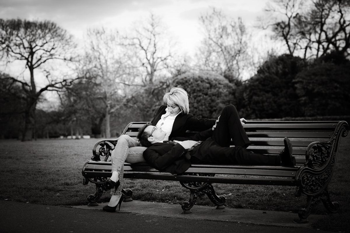 Black and white photo of a person relaxing on a park bench among bare trees in a serene outdoor setting.