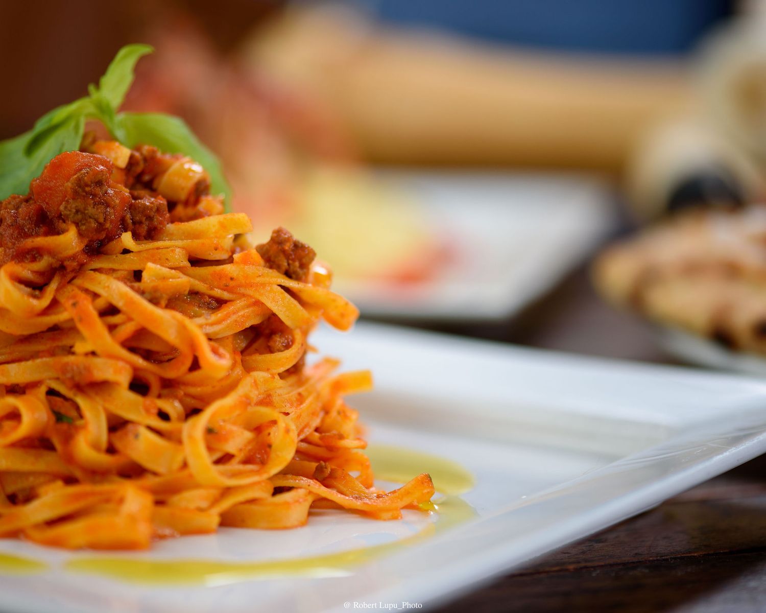 Fettuccine pasta with bolognese meat sauce topped with fresh basil on a white plate.