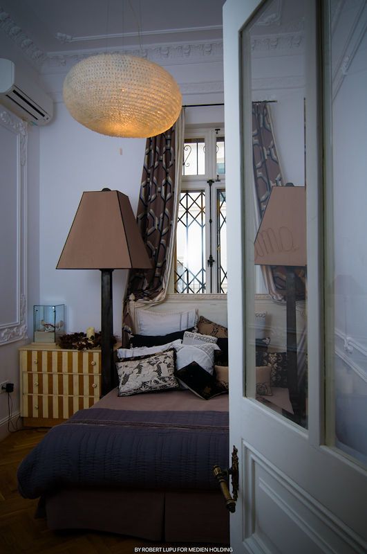 Cozy bedroom with pendant light, table lamps, patterned curtains, and a bed with decorative pillows near a window.