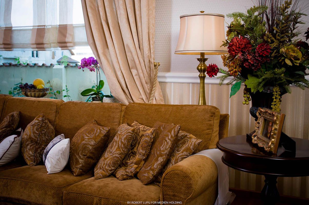 Elegant living room with gold velvet sofa, decorative pillows, brass floor lamp, and floral arrangement on dark side table.