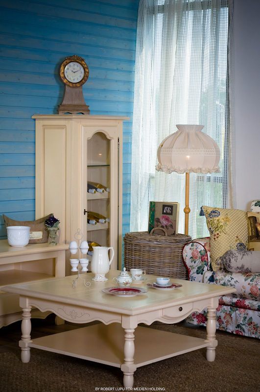 Vintage shabby chic living room with cream coffee table, floral armchair, blue wood walls, and antique cabinet with clock.
