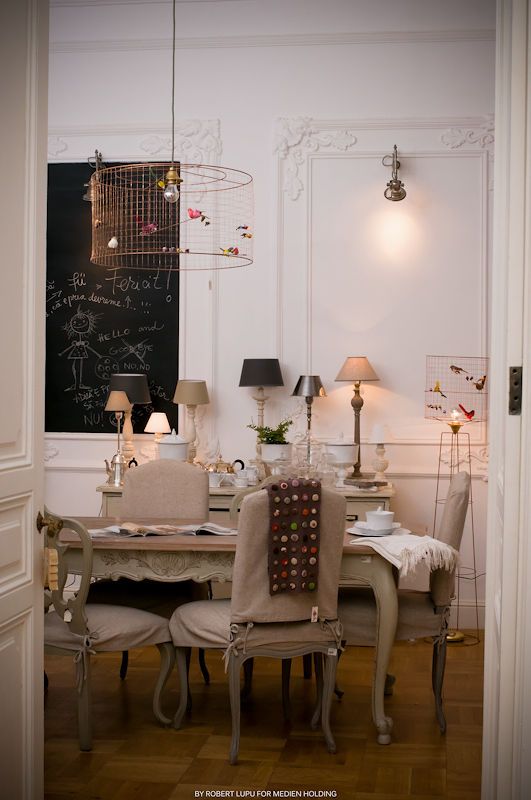 Elegant French dining room with ornate chairs, chalkboard wall, chandelier, and table lamps in a white molding interior.