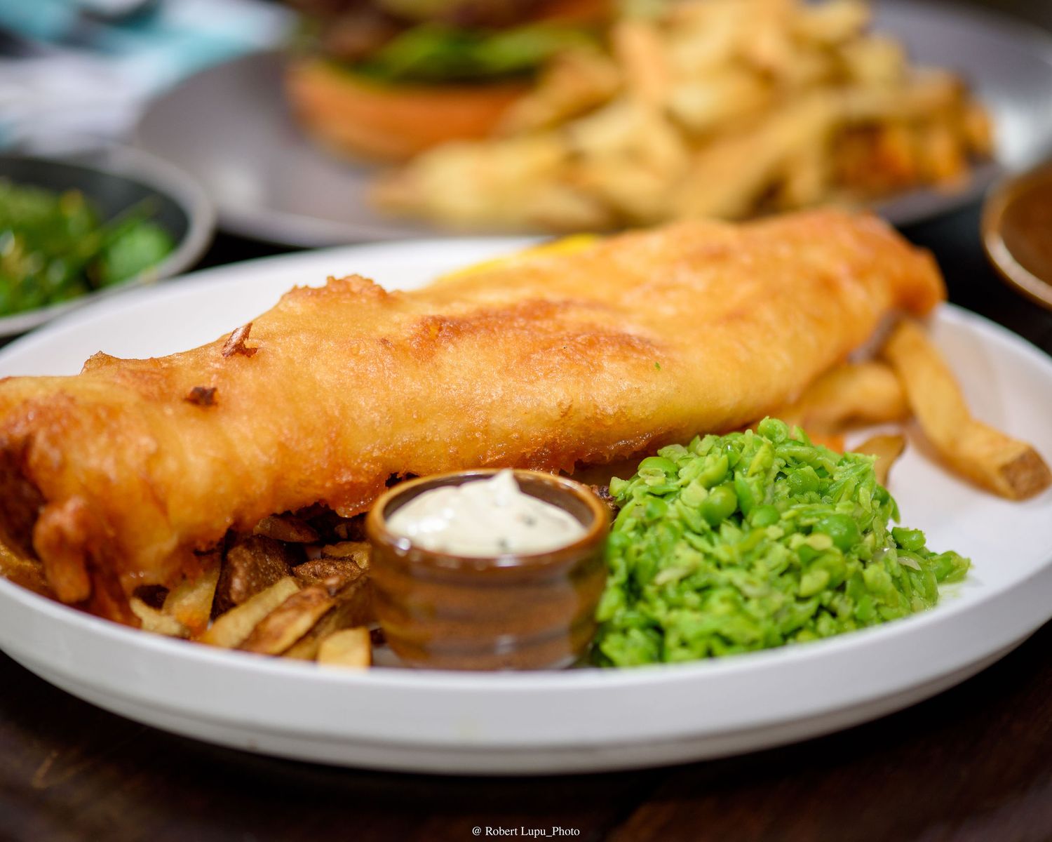 Classic British fish and chips with mushy peas, tartar sauce, and golden battered cod on a white plate.