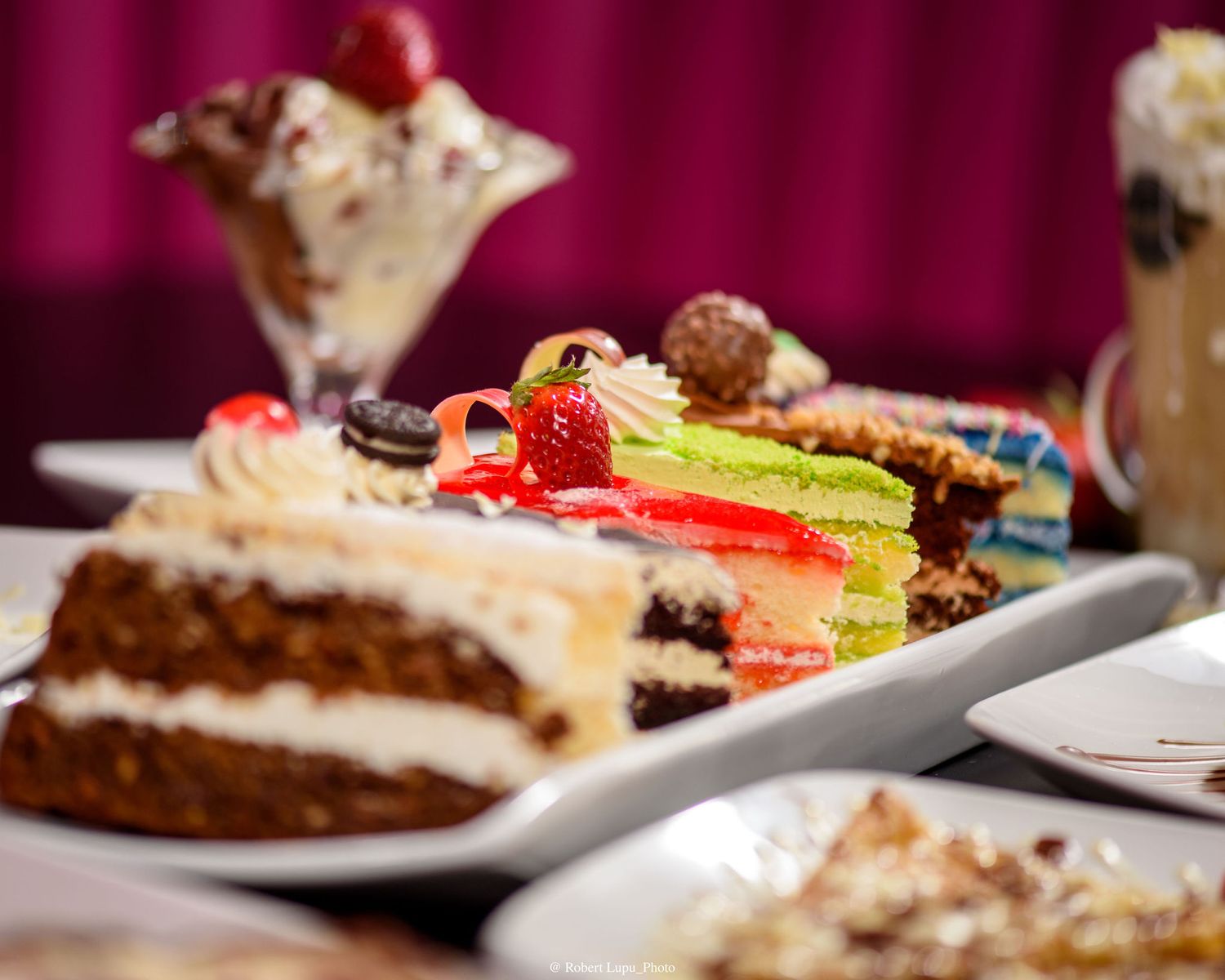 Assorted dessert slices including carrot cake and layered cakes with fresh strawberries on a white plate.