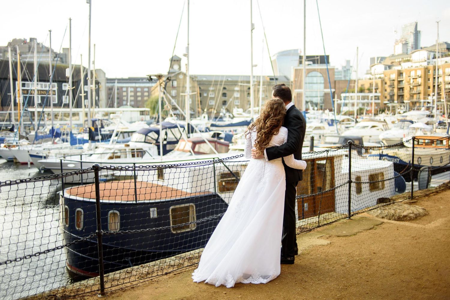 Bride and groom embrace overlooking a marina with yachts and city buildings on their wedding day.