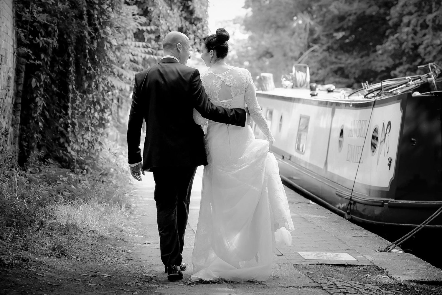 Bride and groom walking hand in hand along a canal path in black and white wedding photography.