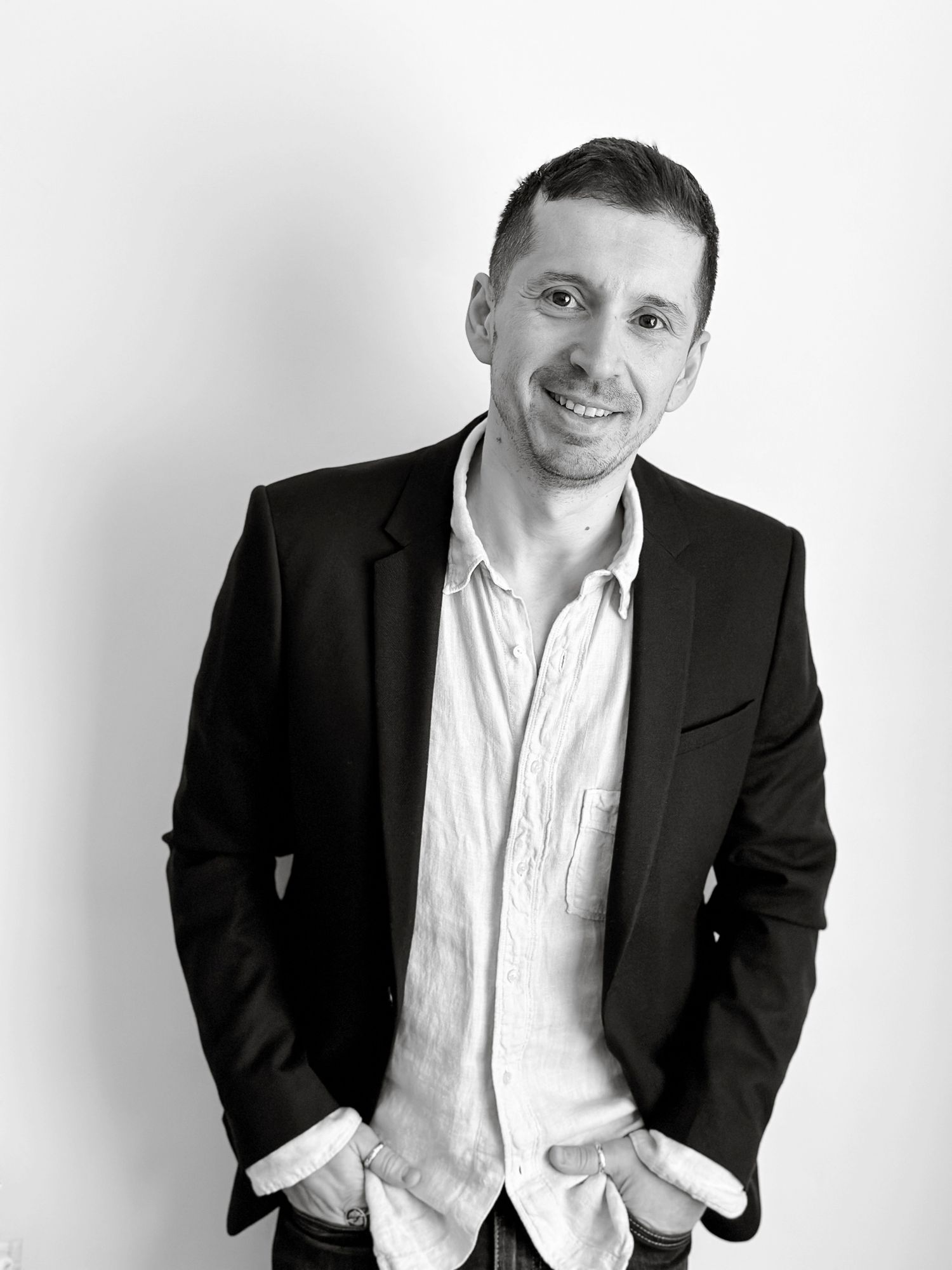 Smiling man in black blazer and white shirt posing confidently in a black and white portrait.