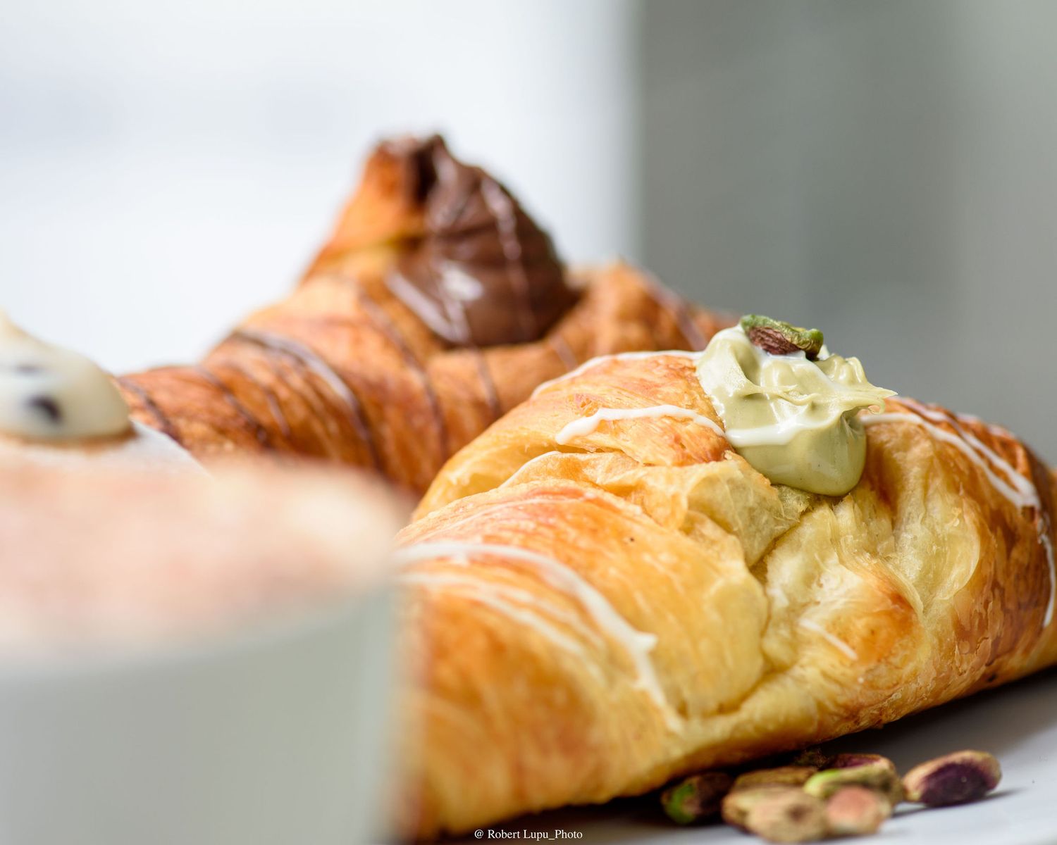 Two golden croissants filled with Nutella and pistachio cream, garnished with pistachios on a white surface.