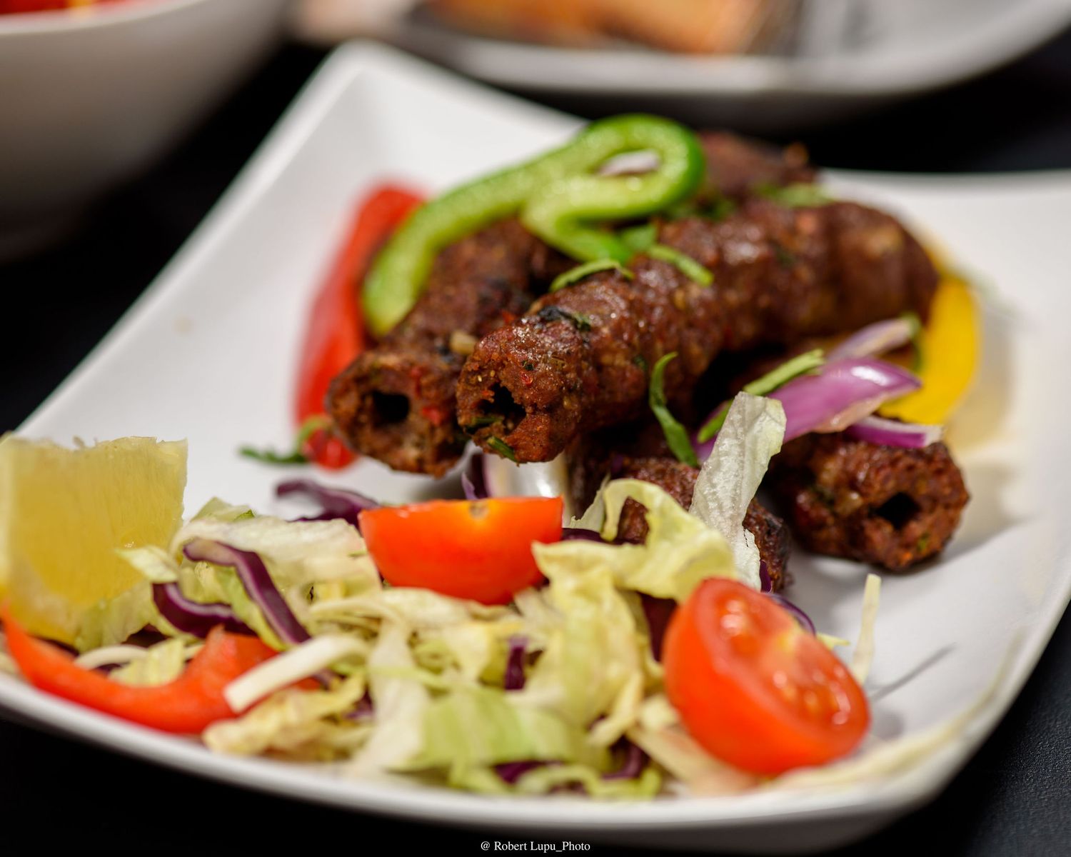 Grilled seekh kebabs served on a white plate with fresh salad, cherry tomatoes, and colorful bell peppers.
