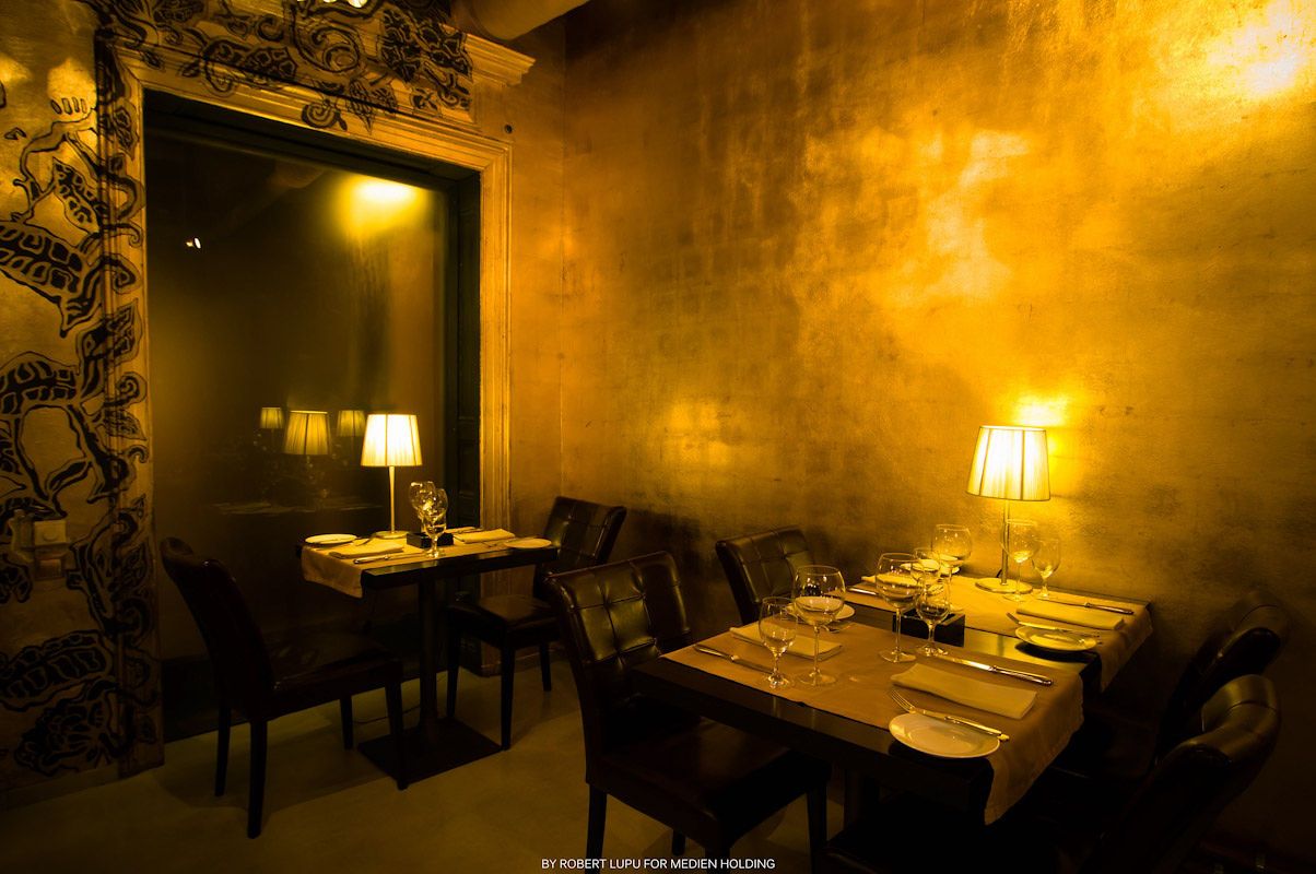 Elegant restaurant dining room with golden walls, dim lighting, and neatly set tables with chairs.