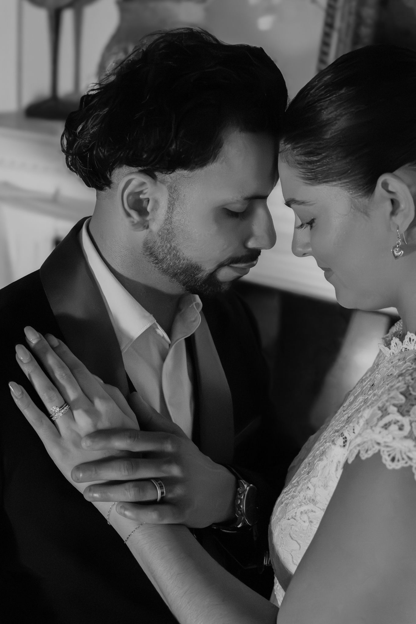 Black and white portrait of a bride and groom touching forereads in a tender moment, her hand with wedding ring resting on his chest.
