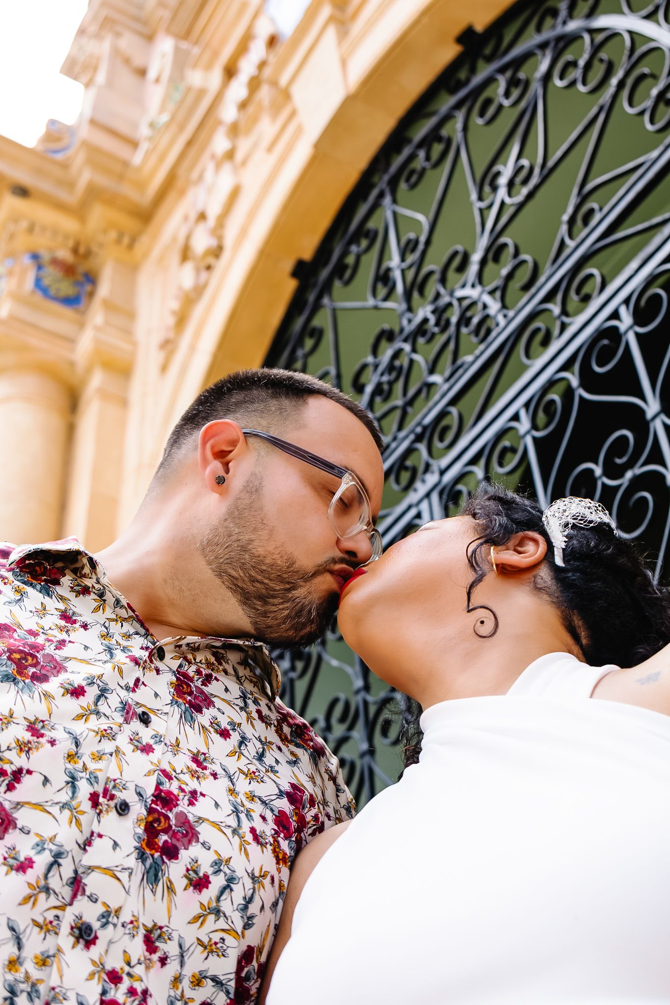Bride and groom sharing a kiss in front of decorative wrought iron gates at their outdoor wedding.