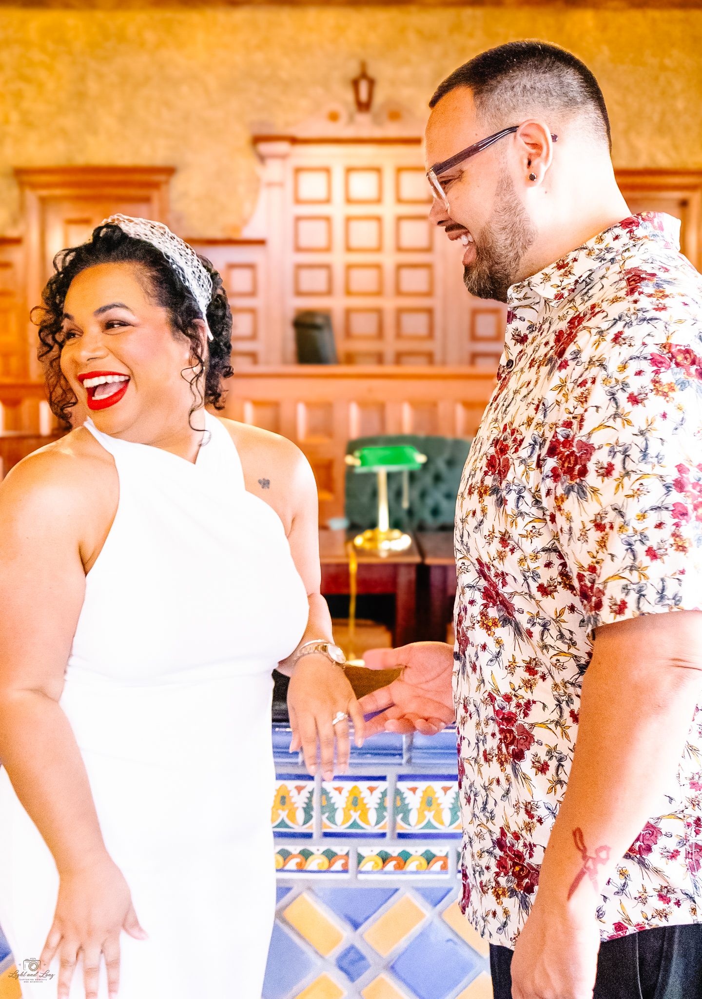 Joyful bride in white halter dress laughing with groom in floral shirt at their courthouse wedding.