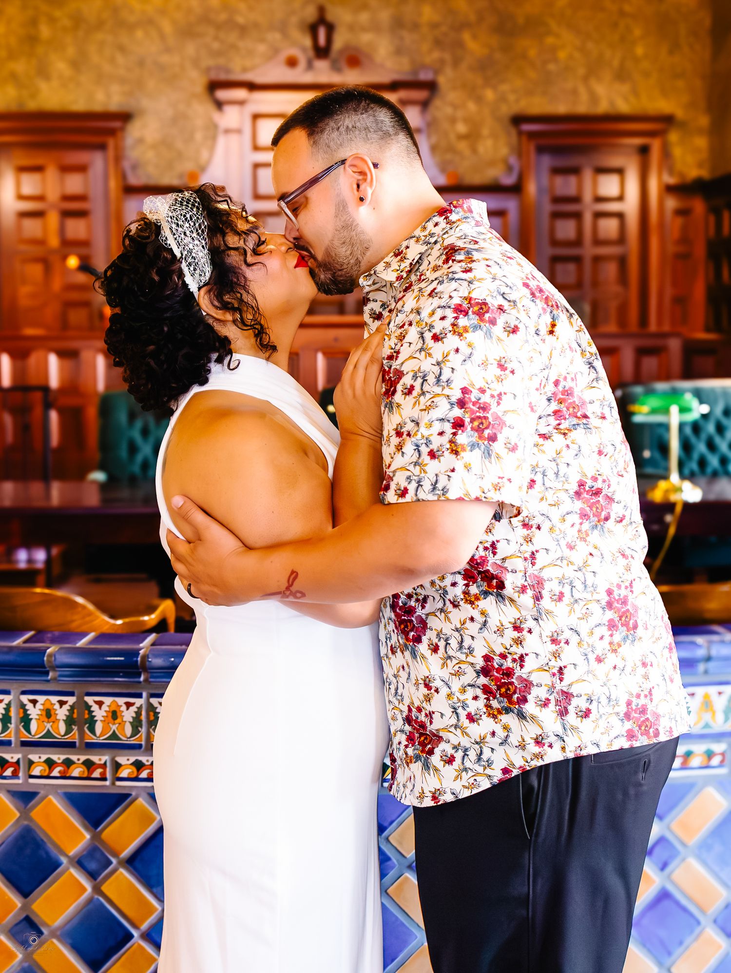 Newlyweds sharing a romantic kiss inside a beautifully decorated courthouse with colorful tile accents.