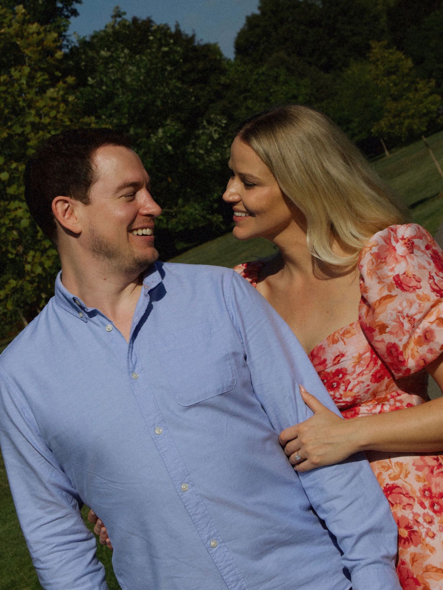 Couple smiling at each other outdoors in warm sunlight, capturing a candid and joyful moment
