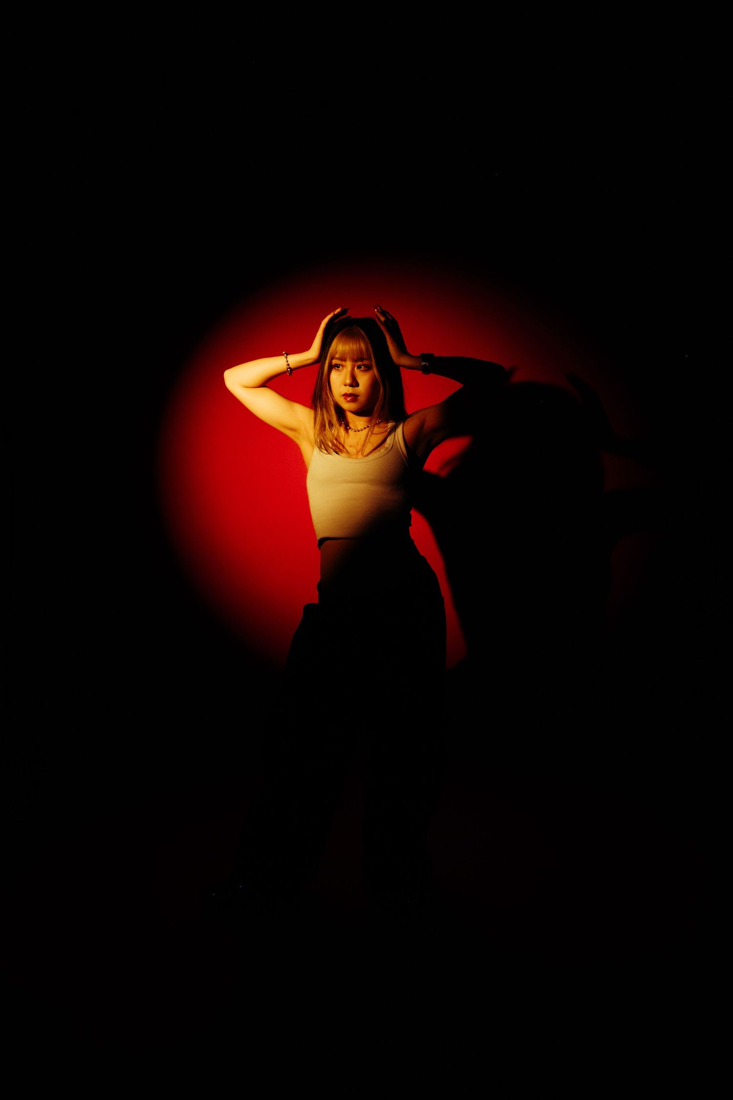 Young woman in white top poses dramatically against a glowing red circular light on a dark black background.