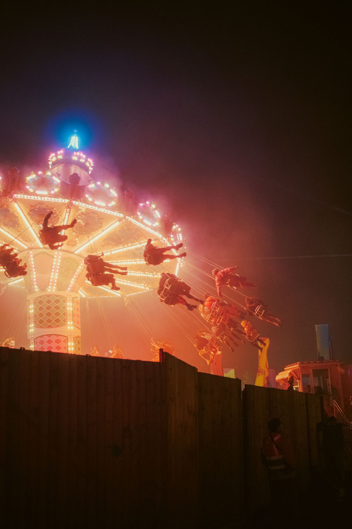 Illuminated carnival swing ride spins riders through foggy night sky at a vibrant outdoor fairground.