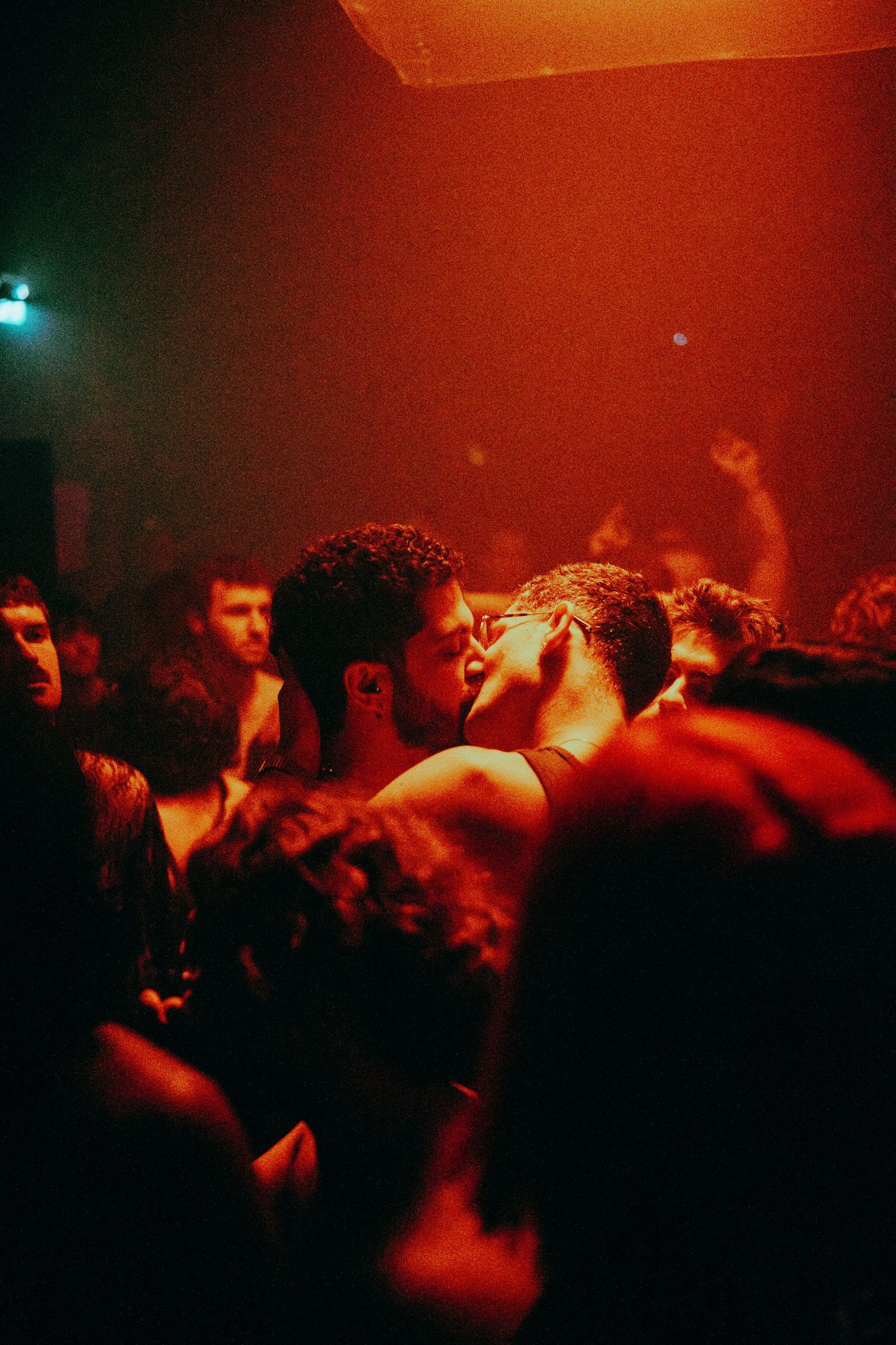 Crowd of people dancing closely together under warm red lighting at a packed nightclub party.
