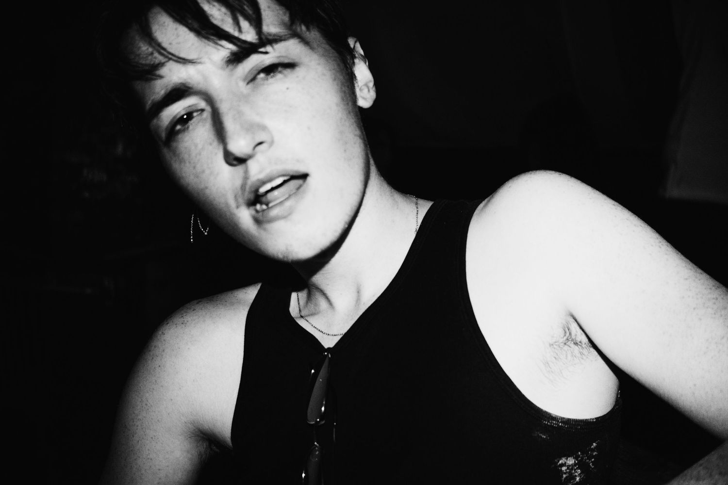 Black and white close-up portrait of a young person with wet hair in a dark, moody setting.