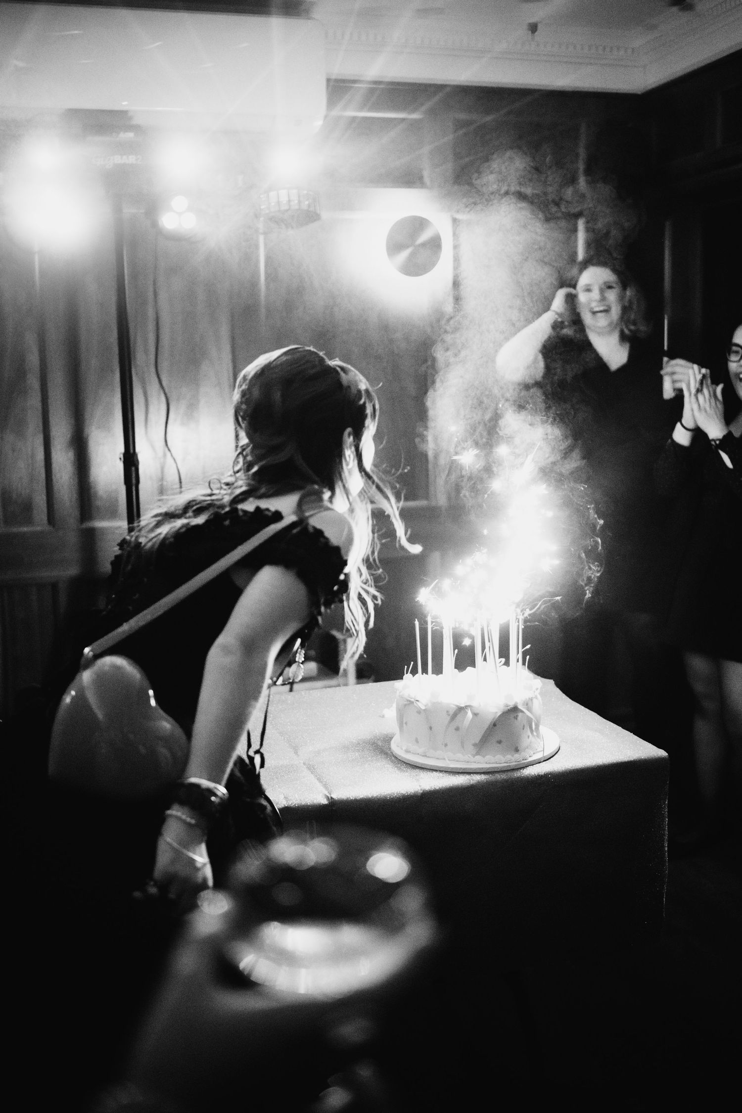 Woman blowing out sparkling birthday cake candles at a celebration in black and white photography.