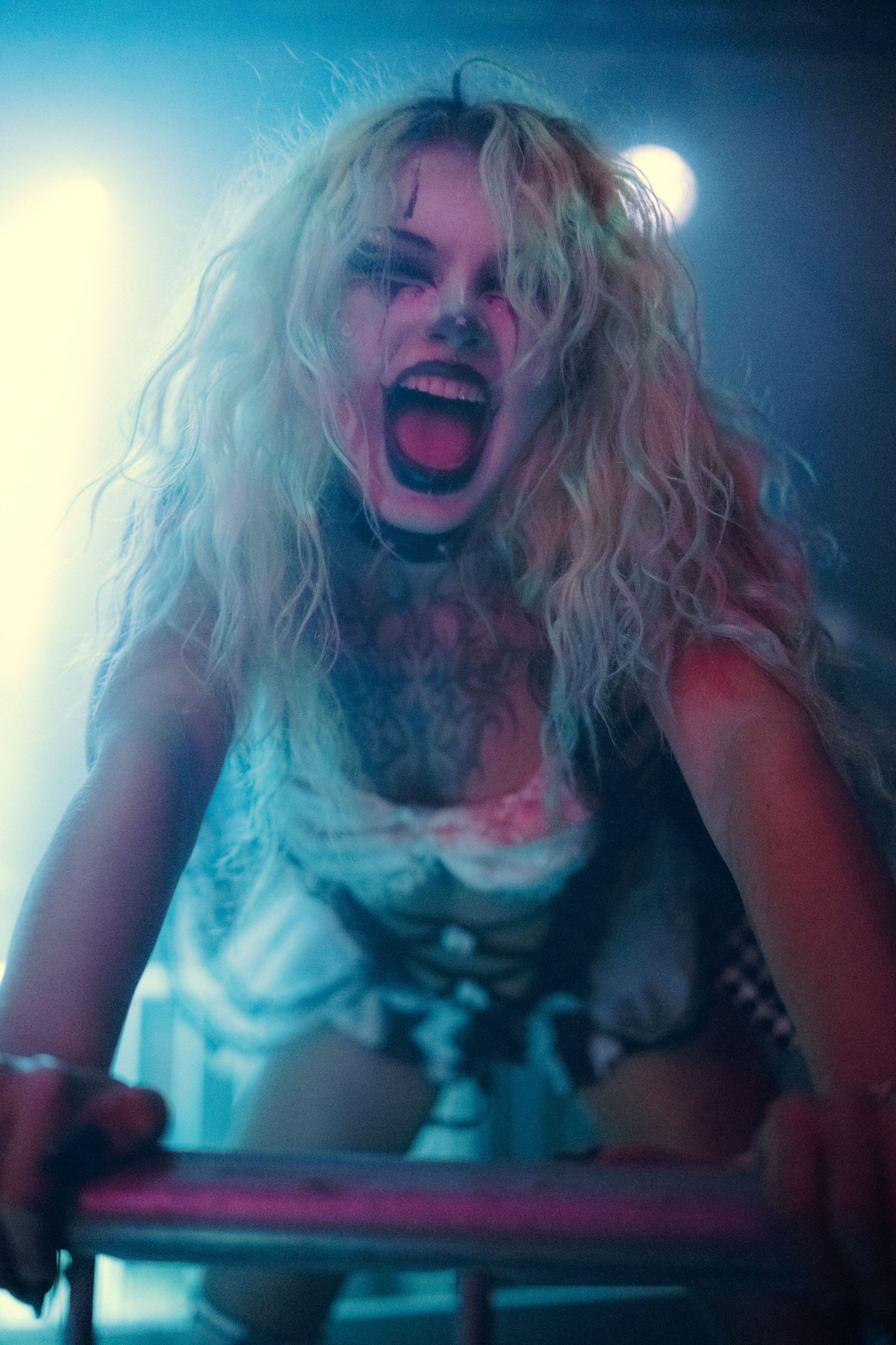Blonde woman in zombie Halloween makeup screaming aggressively under stage lights.