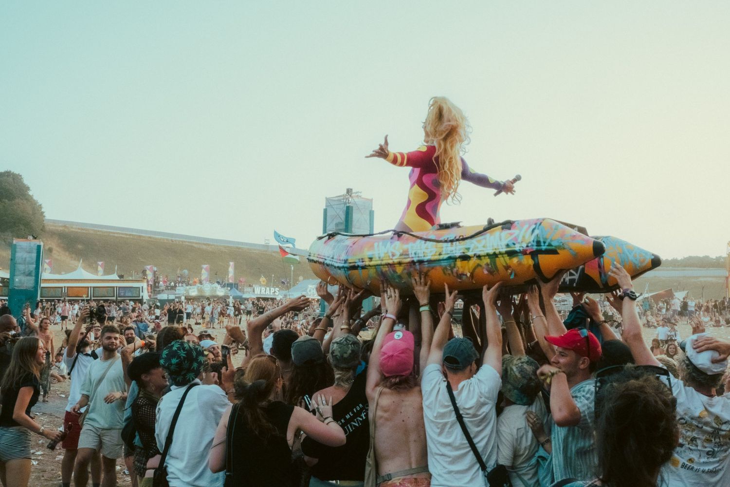 Crowd surfs a woman in colorful outfit on an inflatable raft at a lively outdoor music festival.