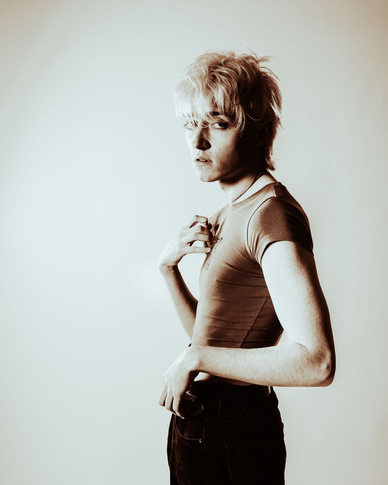 A person with short blonde hair poses in profile wearing a ribbed tank top against a light background.