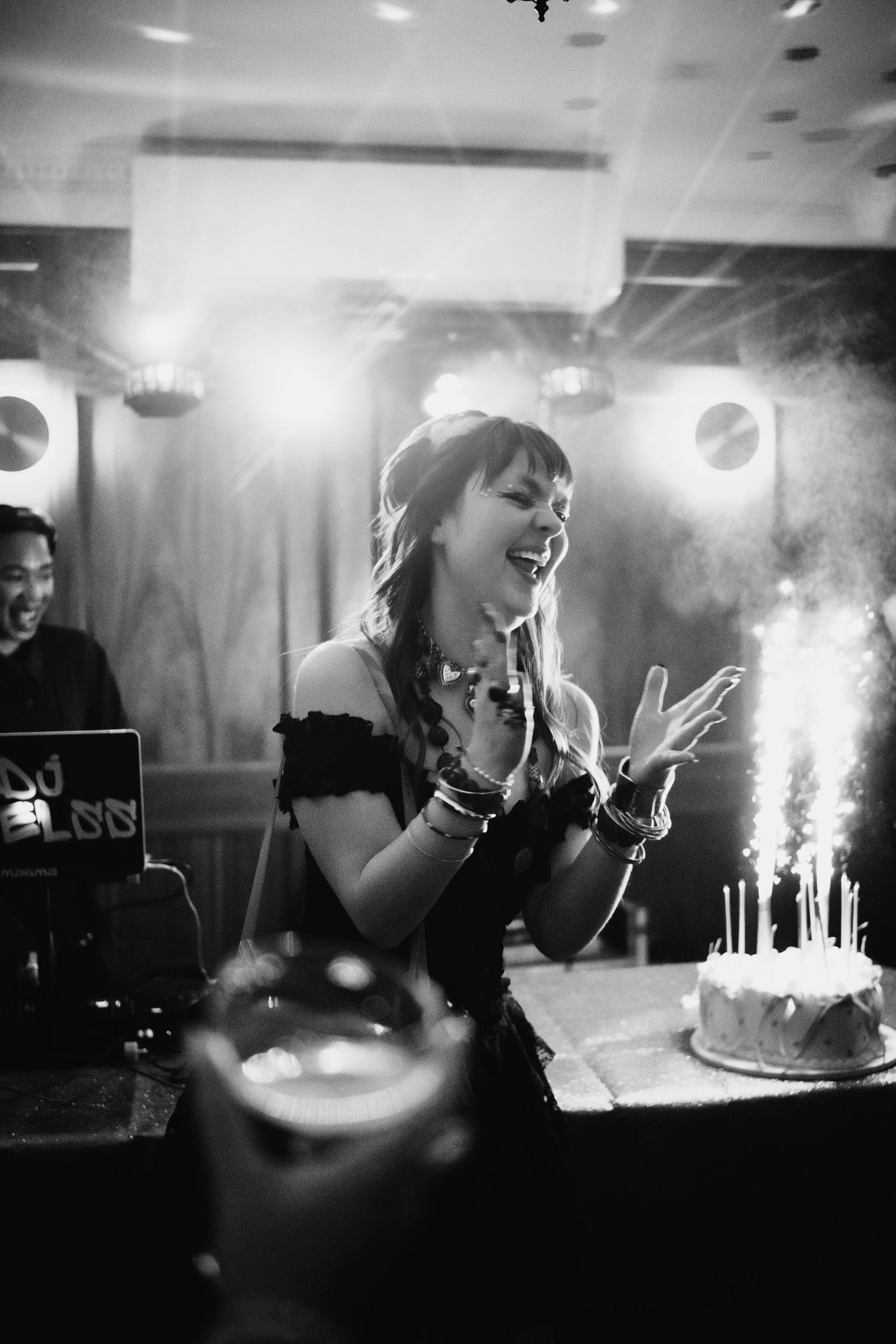 Woman laughing joyfully beside a birthday cake with sparkler candles in black and white photo.