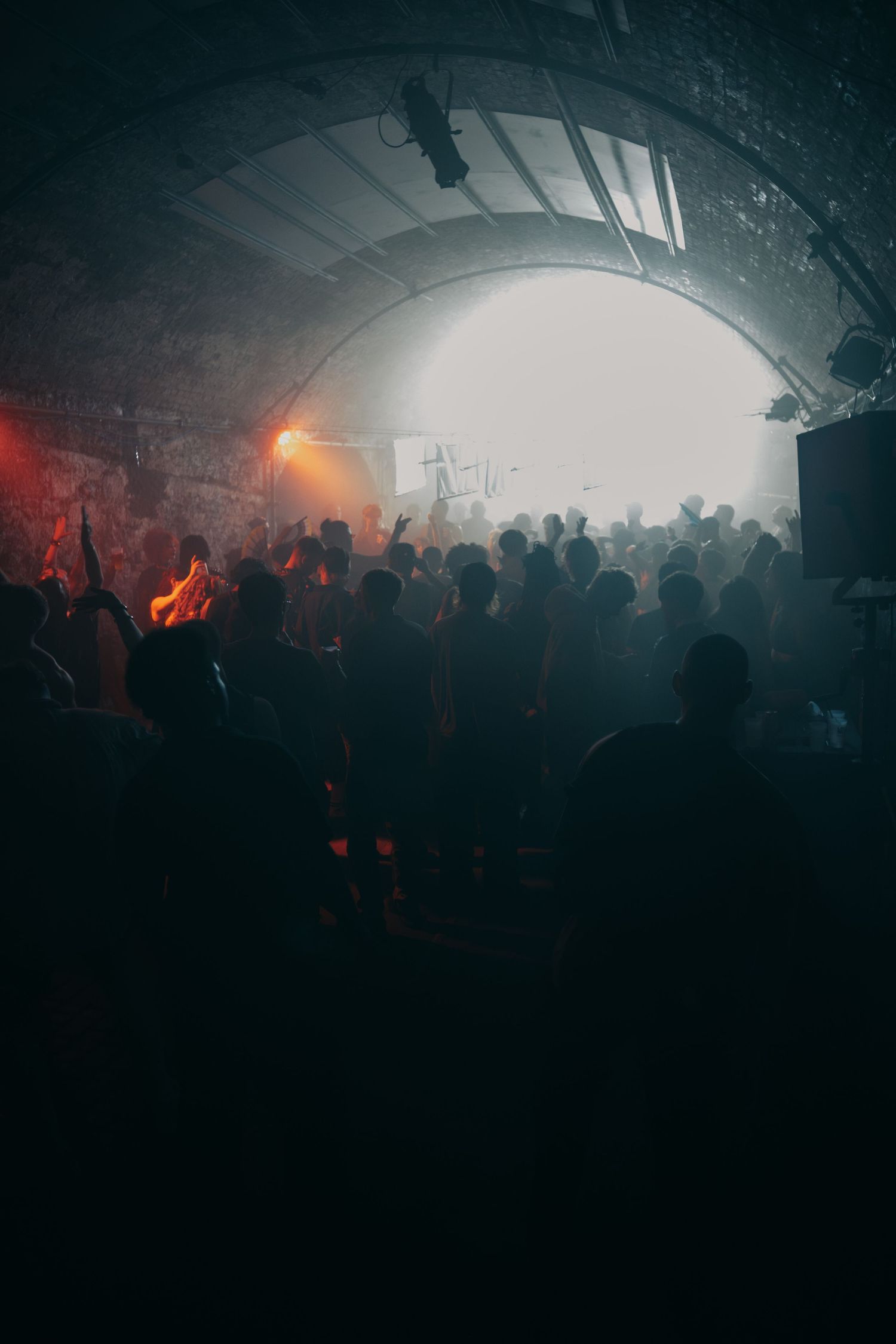 Crowd of silhouettes dancing in a dark tunnel venue with hazy atmospheric lighting.