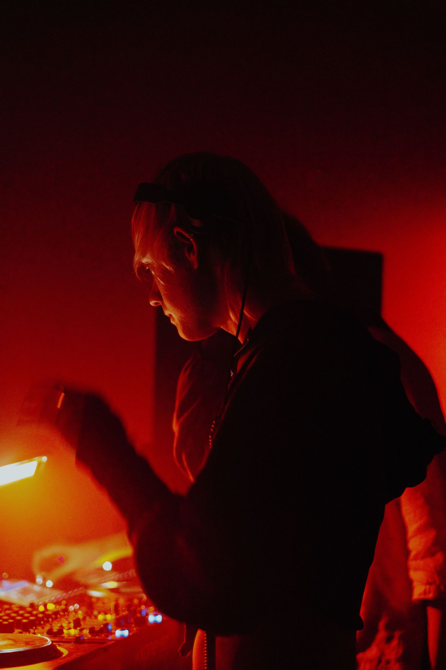 DJ mixing music at turntables bathed in dramatic red lighting at a nightclub event.