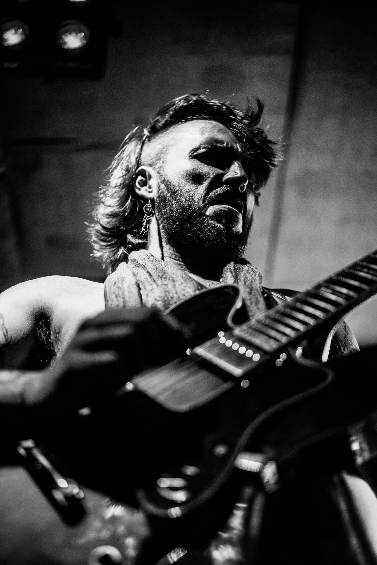 Black and white close-up of bearded male guitarist performing intensely on stage.