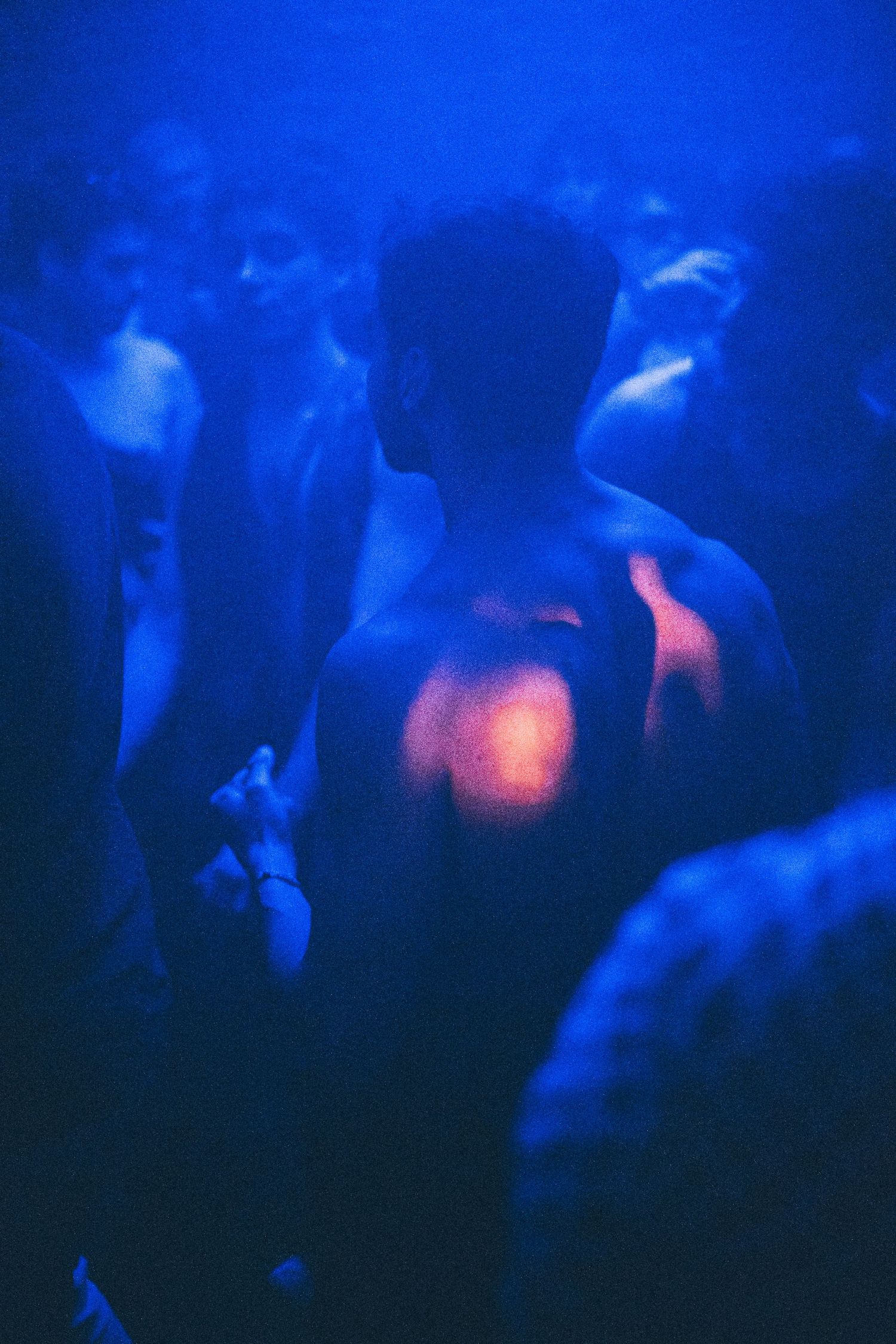 Shirtless man dancing in a crowd under blue and red neon lights at a nightclub.