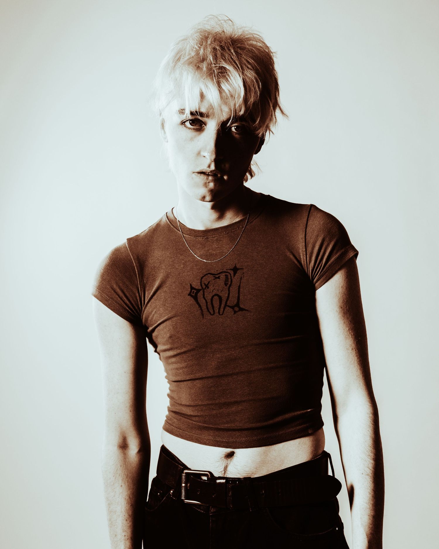 Person with short blonde hair in brown crop tee and black jeans, retro style.