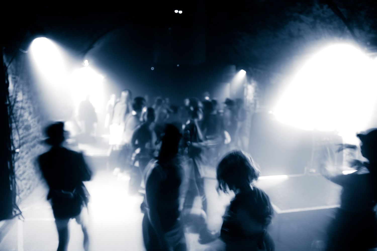 Blurred crowd of dancers moving under bright stage lights in a dark nightclub atmosphere.