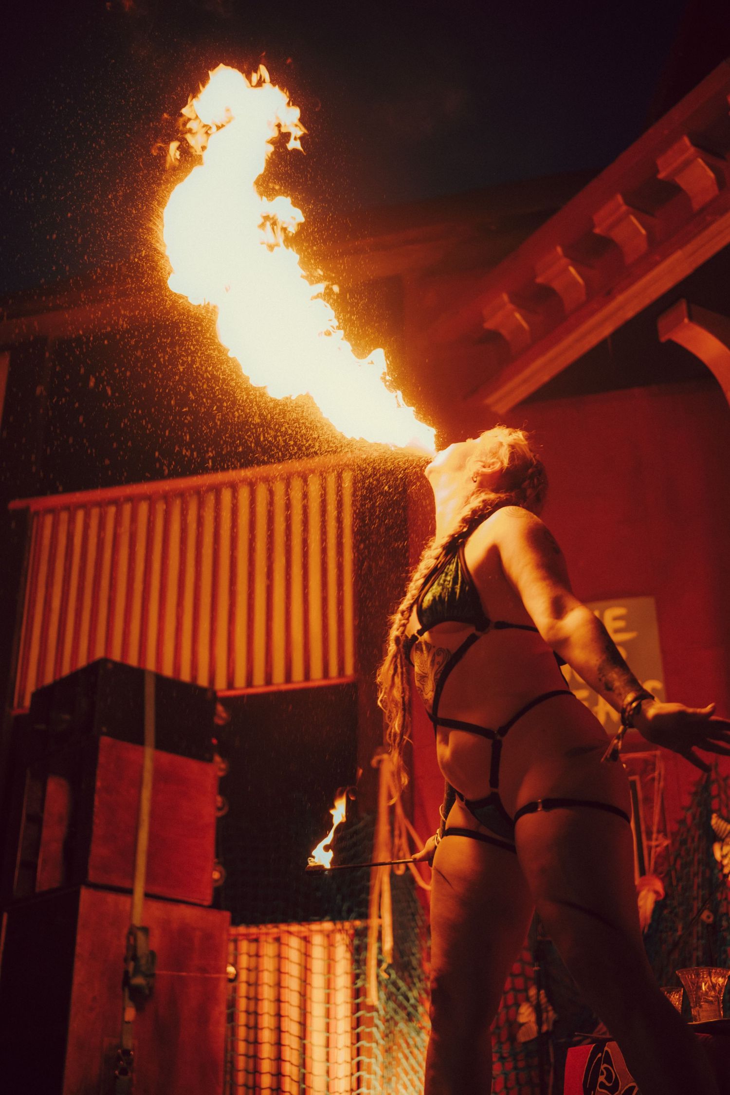 Female fire breather performing dramatic fire show at night outdoor event.