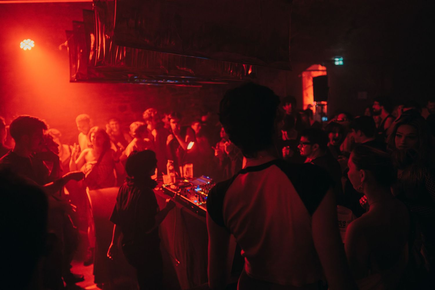 DJ performing for a crowd bathed in red light inside a dark underground nightclub.
