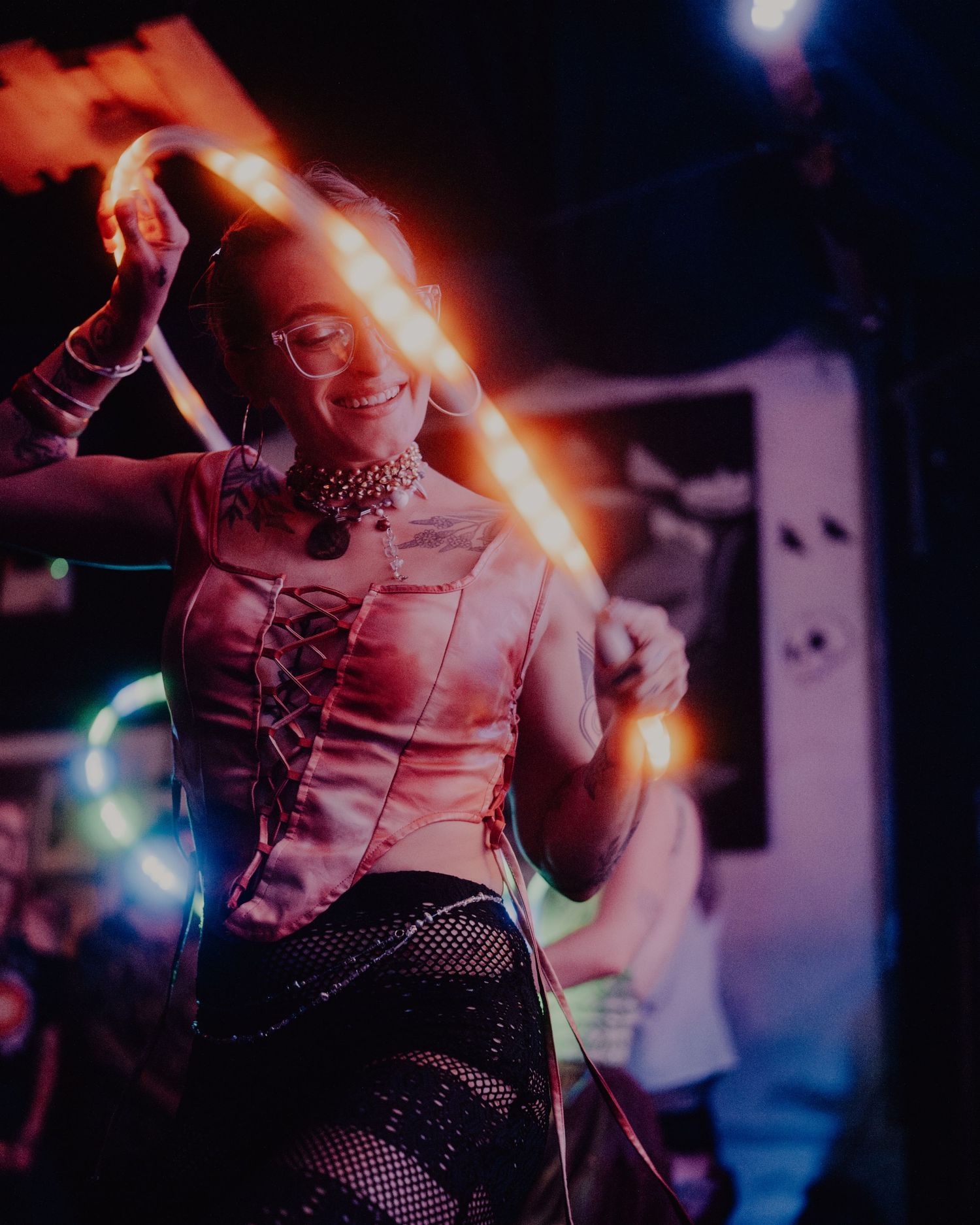 Woman smiling while dancing with glowing light hoop in colorful nightclub setting.