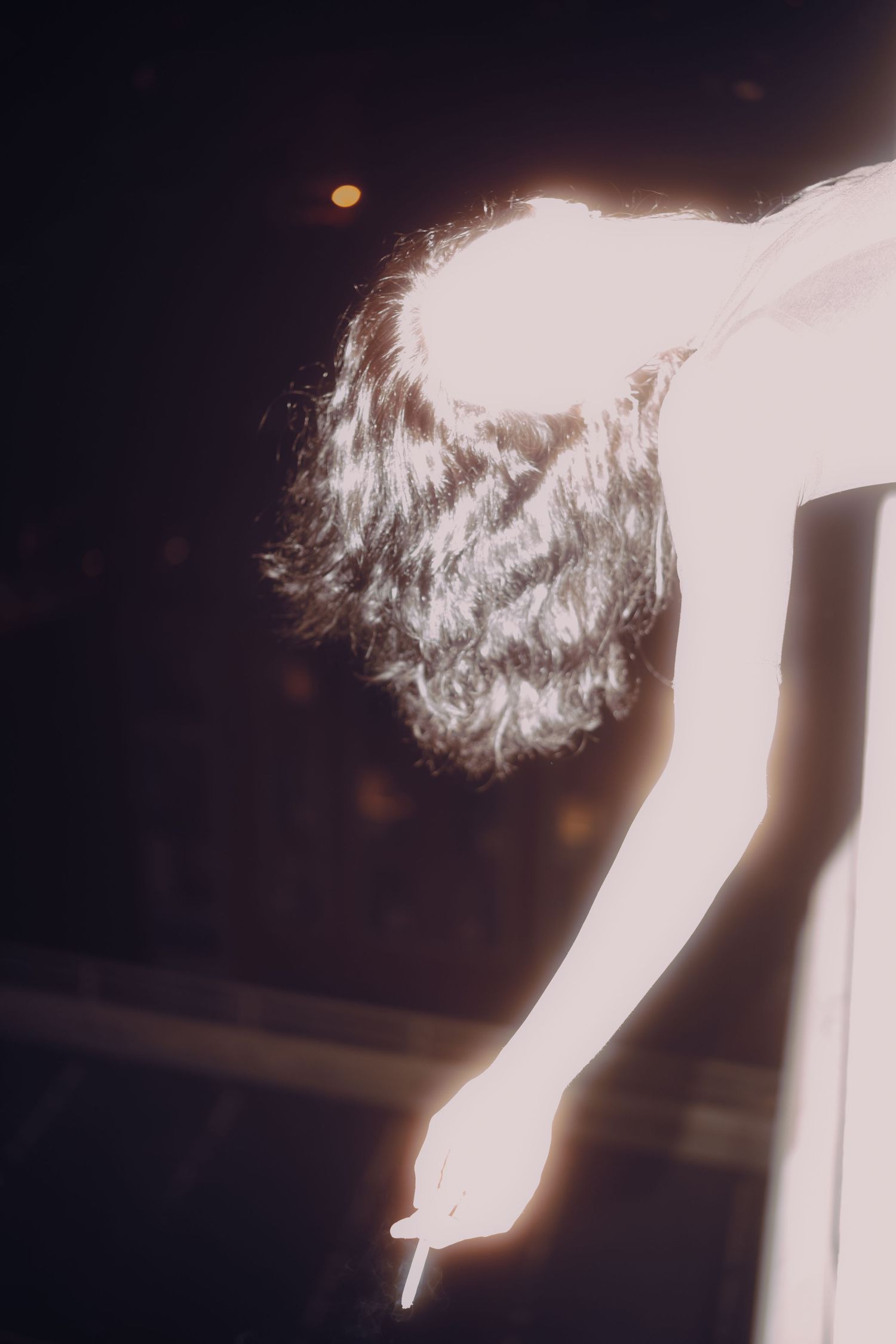 Silhouetted figure with curly hair holding a cigarette in dramatic overexposed light.