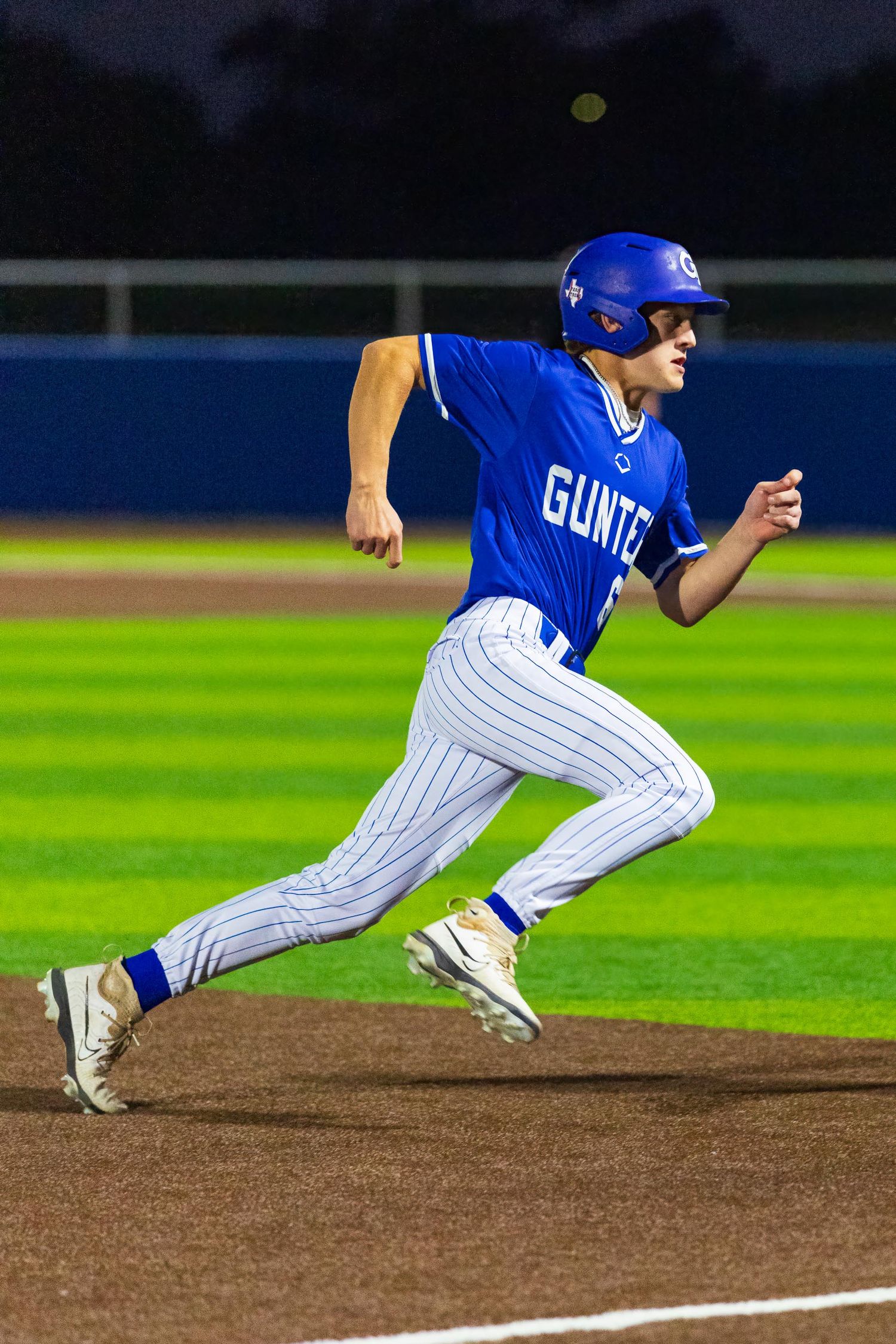 Gunter baseball player in blue uniform sprints along the baseline during a night game.