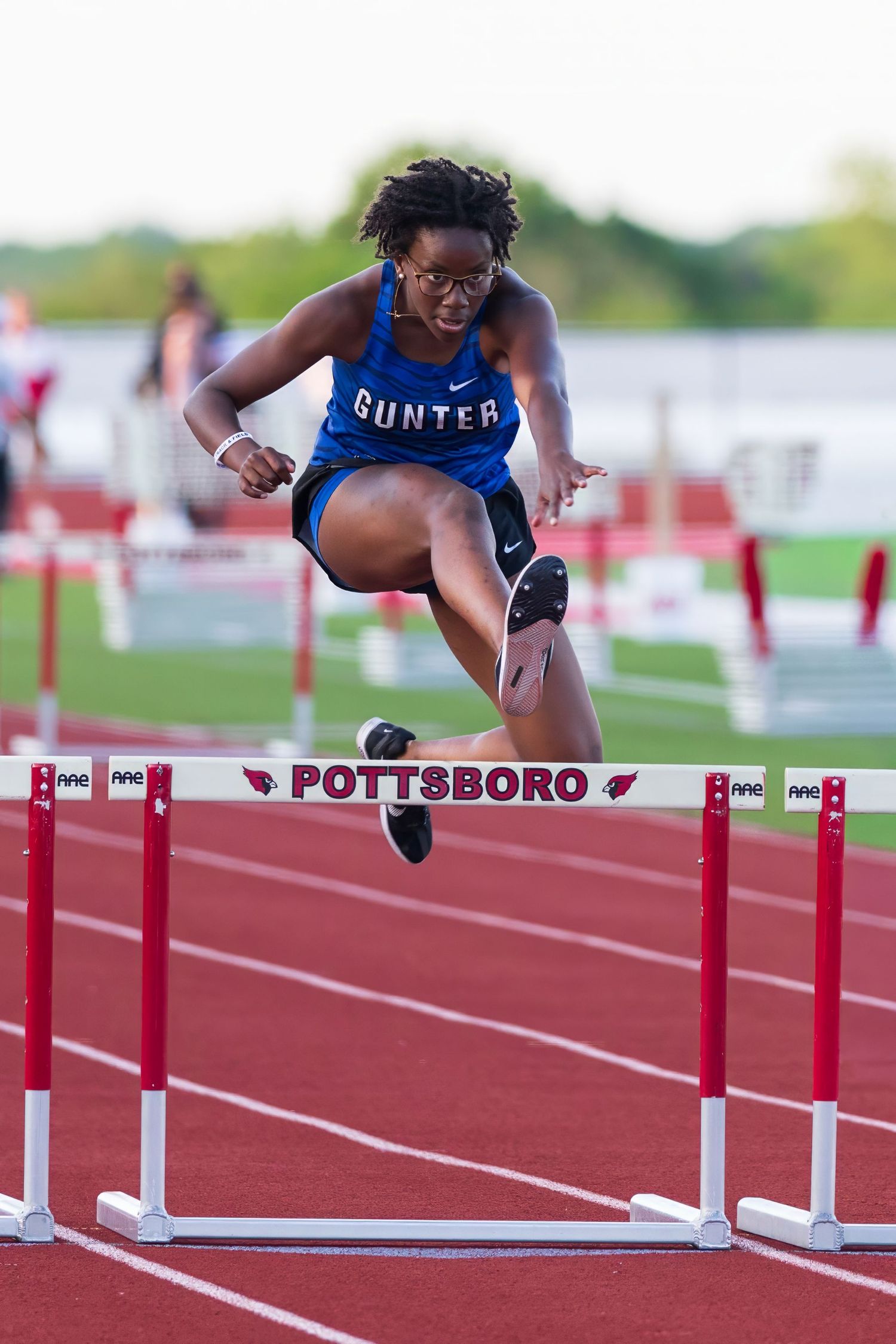 Female Gunter athlete leaps over red hurdles on a Pottsboro track during a competitive hurdles race.