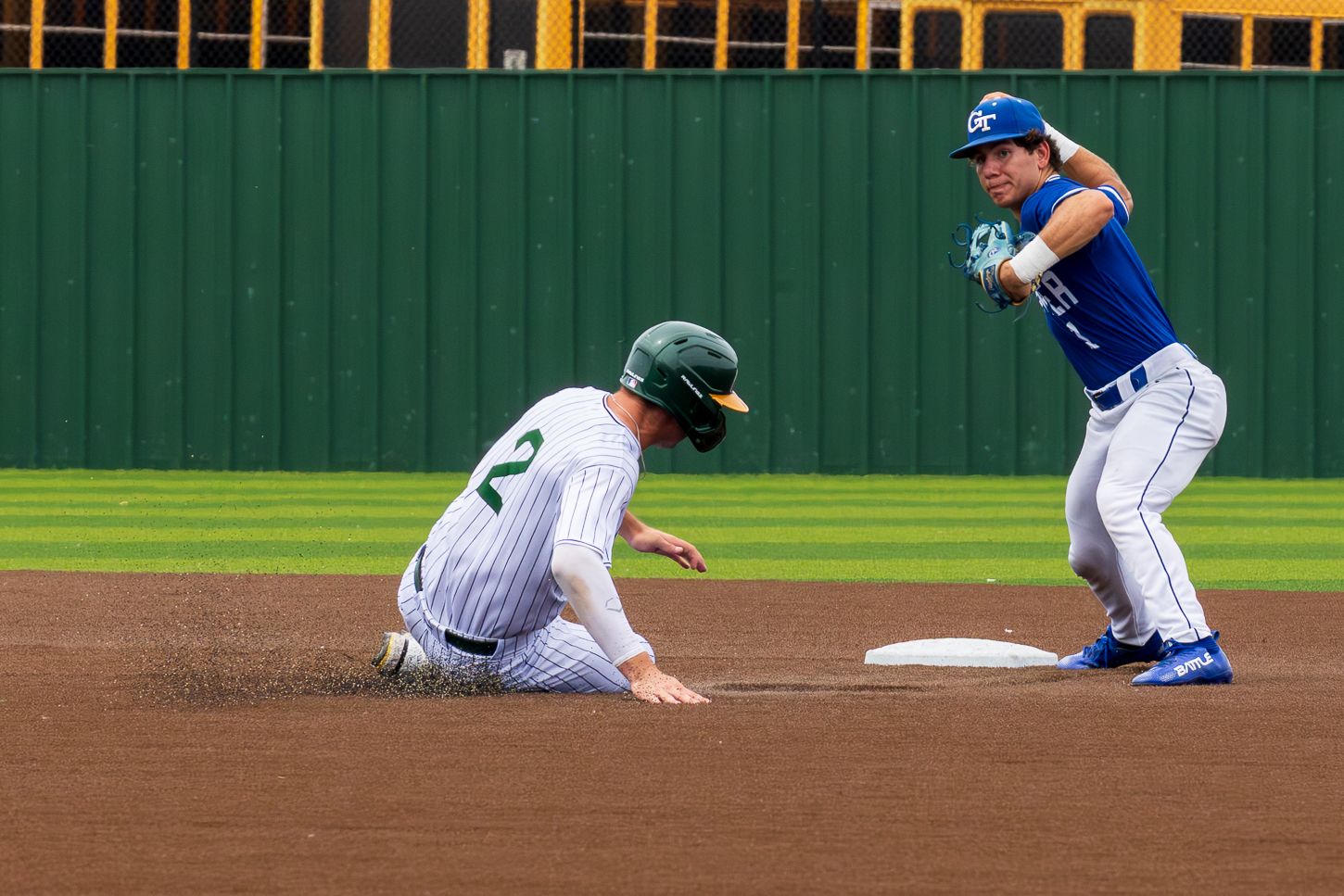 Baseball player slides into second base as infielder in blue uniform attempts to make the tag during a game.
